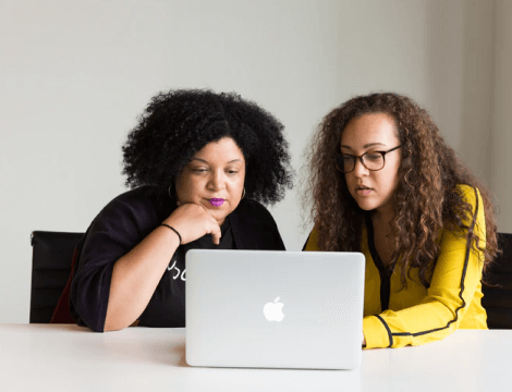 Two business loan agents reviewing online applications together on a computer screen in a modern office.