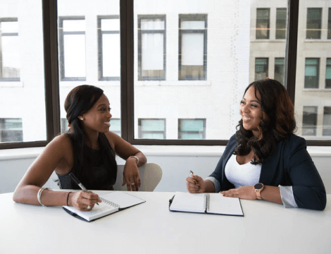 Two loan agents sitting at a desk discussing business loans for international applicants while reviewing client applications and loan approvals.