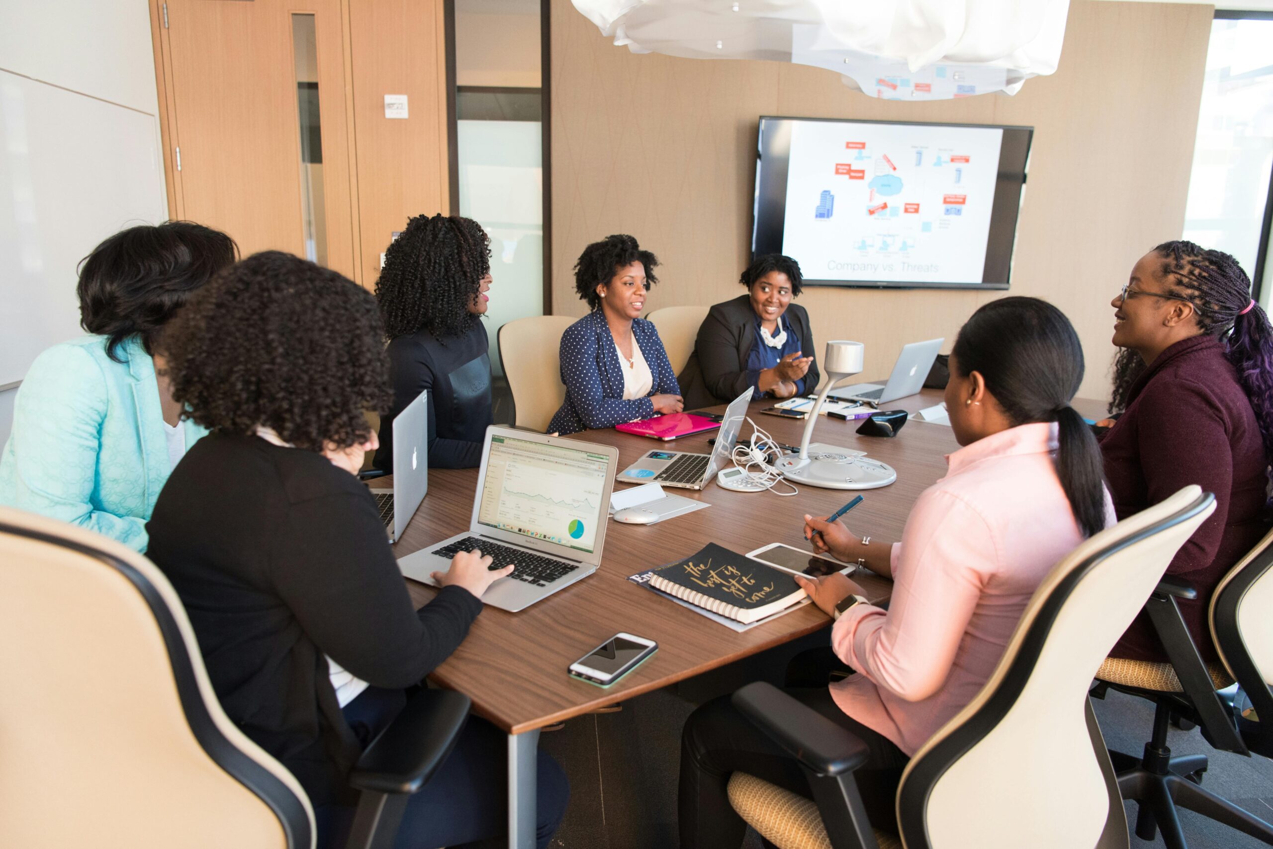 Seven women seated in an office around a table with a laptop, discussing women owned business loans